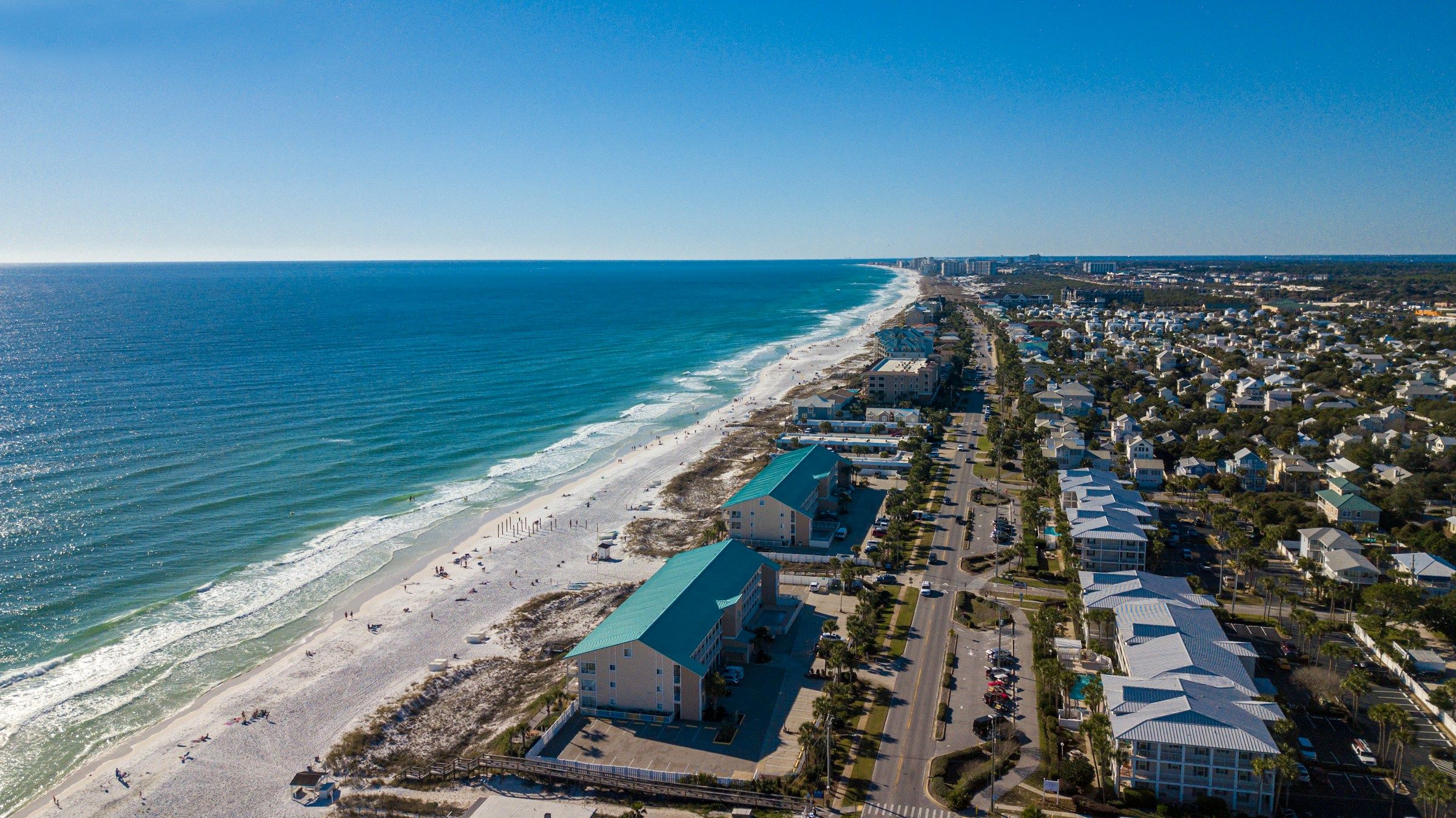 Aerial view of the Destin beachfront: white sand, emerald water and beach houses along the coast road